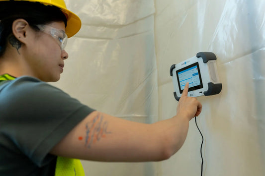 G720 differential pressure monitor monitoring pressure in a containment space. Woman is navigating the digital control screen, while the Omni IQ is affixed to the a containment wall.