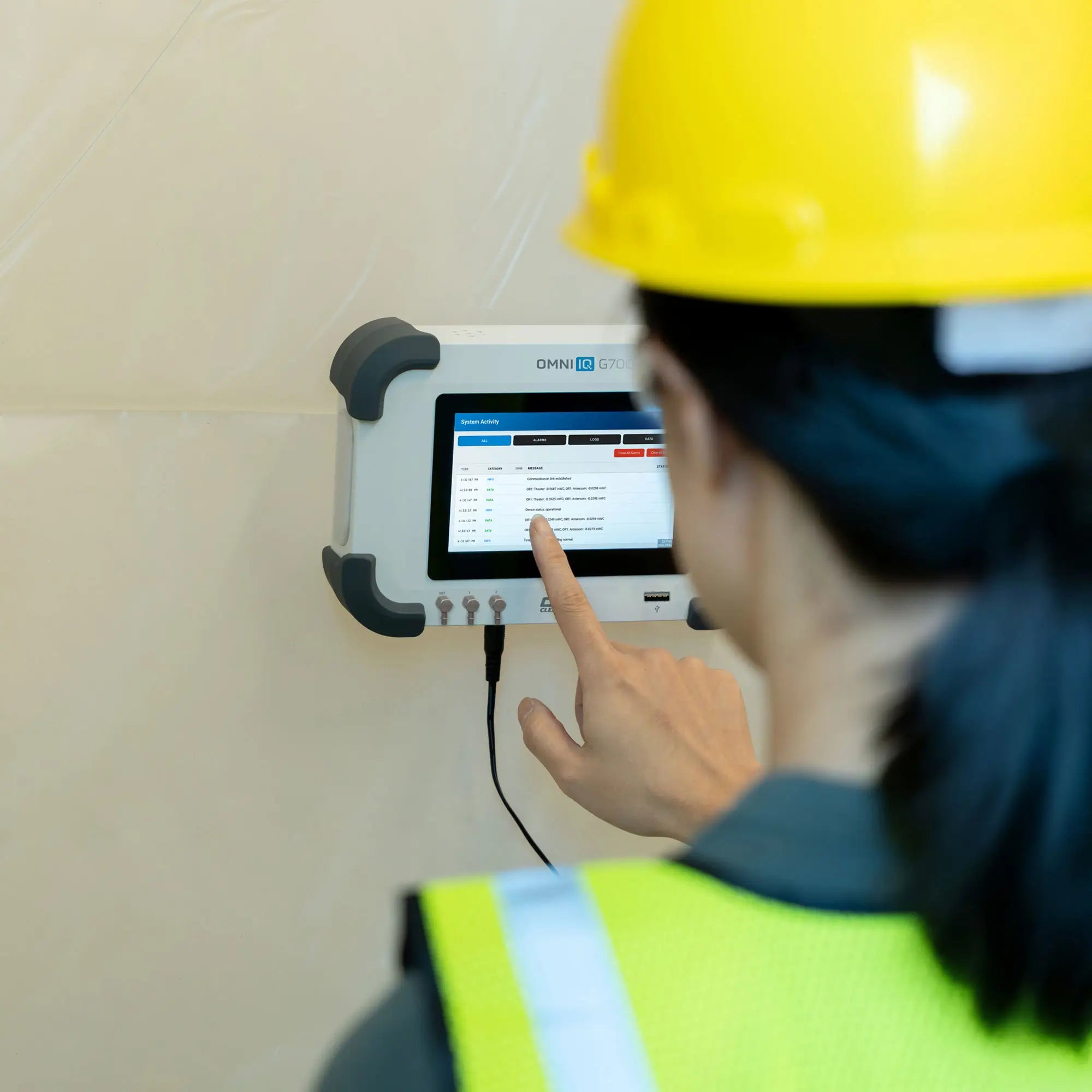 Person in a hard hat and high-visibility vest using an Omni IQ G700 device on a wall.